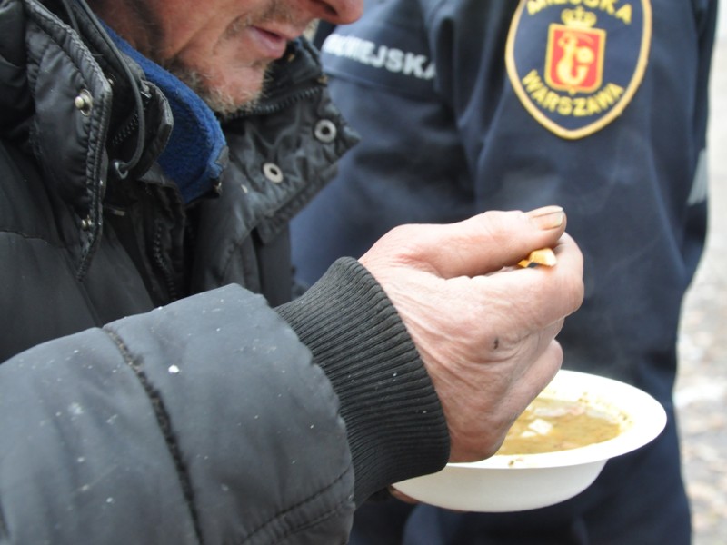 Bezdomny mężczyzna jedzący zupę przywiezioną przez strażników miejskich