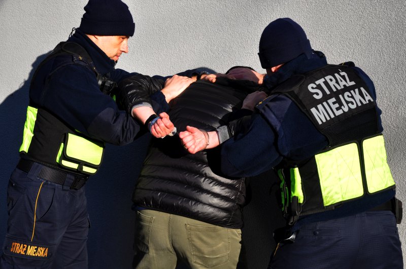 Strażnicy obezwładniają mężczyznę w ciepłej kurtce. Zdjęcie poglądowe.
