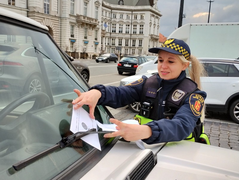 Strażniczka miejska wkładająca ulotkę informacyjną za szybę samochodu