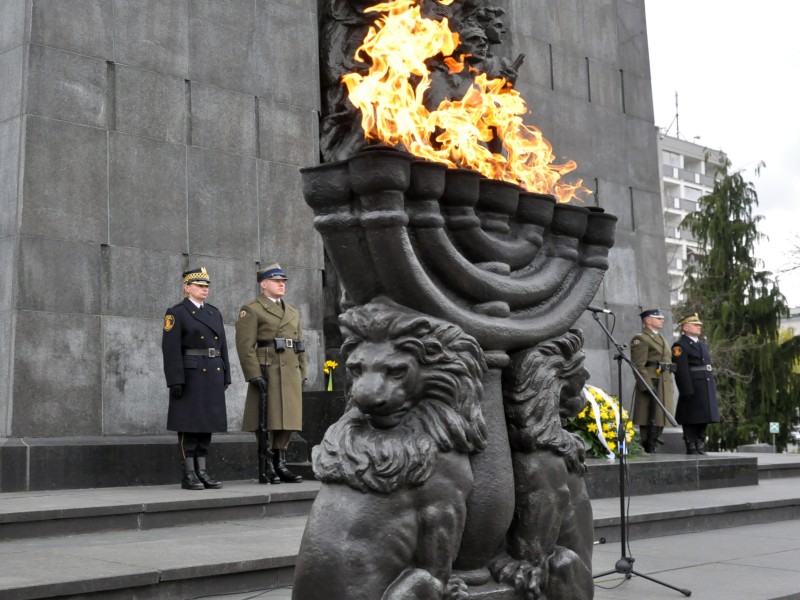 Pomnik Bohaterów Getta. Na pierwszym planie płonący ogień na kamiennej menorze, pod pomnikiem warta honorowa straży miejskiej i wojska.
