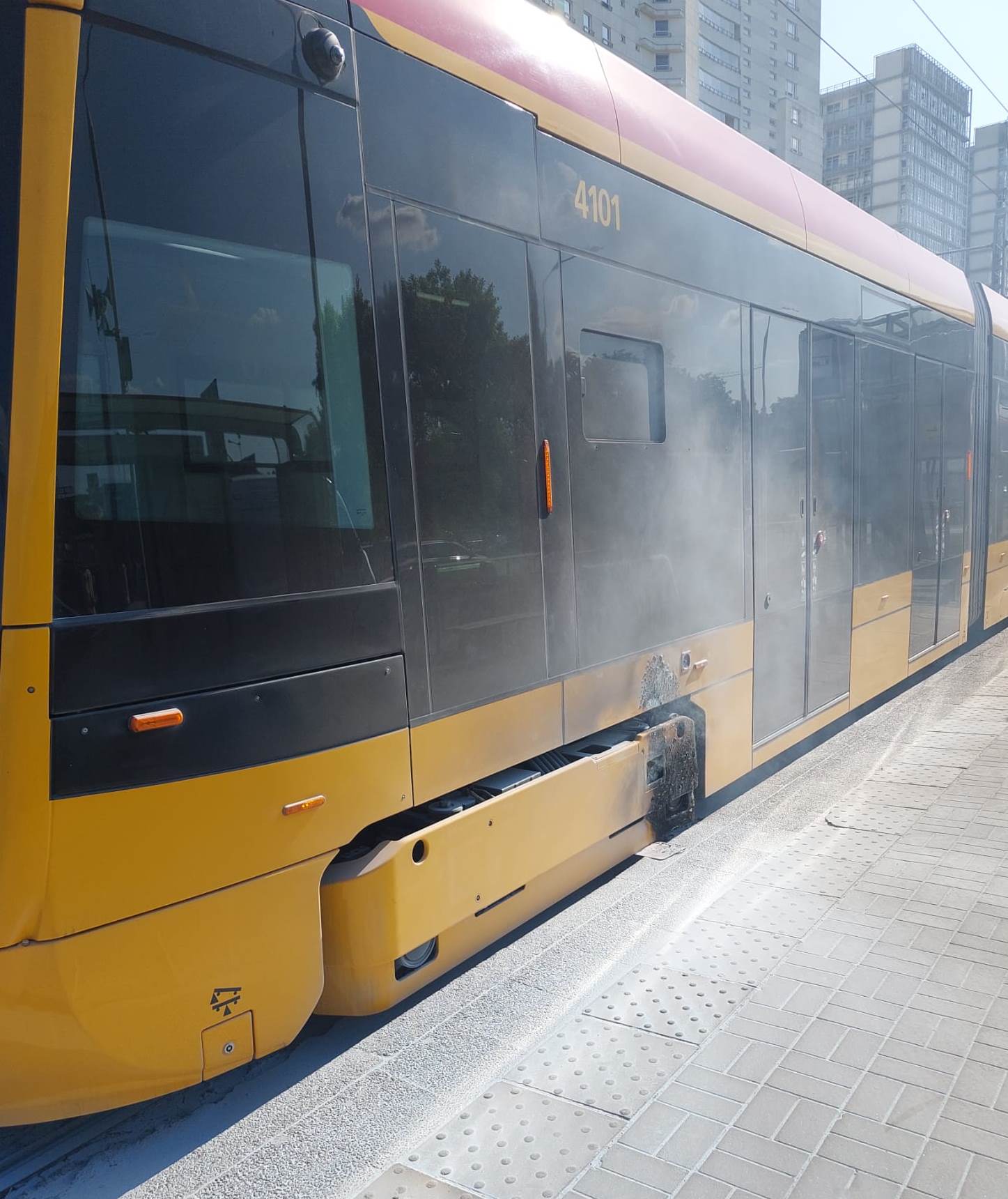 Dym unosi się sponad ugaszonej osi tramwaju, który stoi na przystanku.