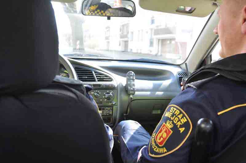 Zdjęcie ilustracyjne: strażnik miejski siedzący w radiowozie na miejscu pasażera.