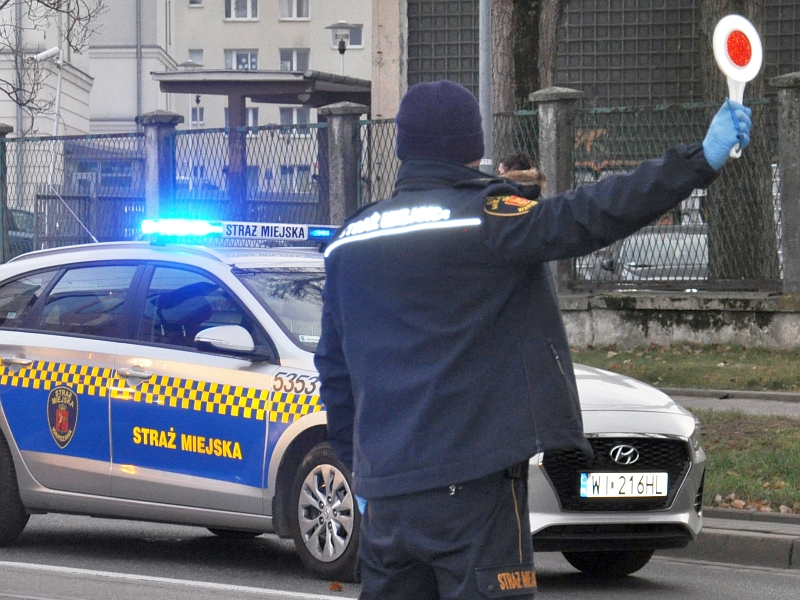 Strażnik miejski podczas zatrzymywania pojazdu do kontroli. W tle radiowóz straży miejskiej- zdjęcie ilustracyjne