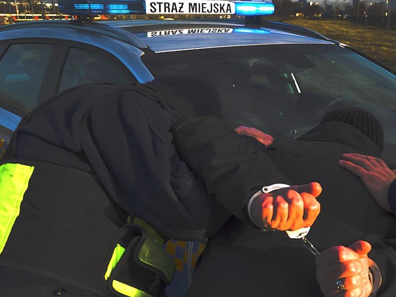 Strażnik przytrzymujący na masce samochodu obezwładnionego, zakutego w kajdanki mężczyznę- zdjęcie ilustracyjne.