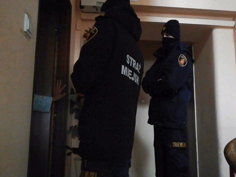Strażnicy miejscy na klatce schodowej przed drzwiami mieszkania- zdjęcie ilustracyjne