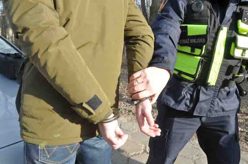 Strażnik miejski przytrzymujący mężczyznę z założonymi kajdankami- zdjęcie ilustracyjne
