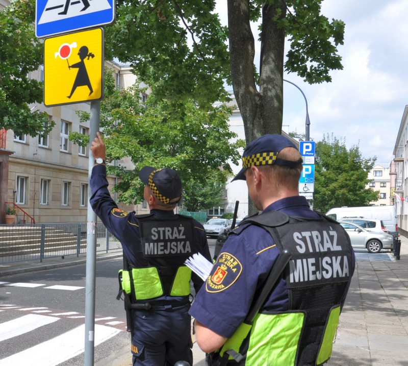 Strażnicy miejscy sprawdzający znaki drogowe przy przejściu dla pieszych w pobliżu szkoły