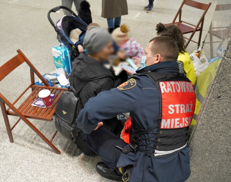 Zdjęcie z jednej z interwencji: strażnik klęczy przy kobiecie z dzieckiem w jednym z punktów informacyjnych w Warszawie.