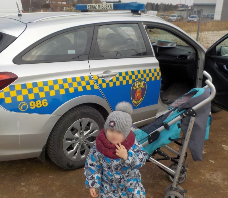 Zdjęcie z interwencji: mały chłopczyk stoi przed swoim nowym wózkiem. W tle radiowóz straży miejskiej.